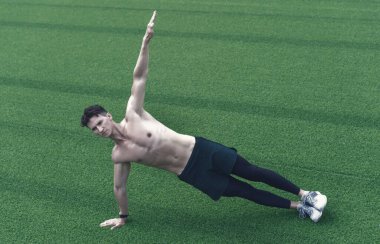 Açık havada spor yapan güçlü bir delikanlı. Çimenlerde yoga yapan bir adam. Spor salonunda spor yapıyorum. Şehirde yoga yap. Yan açı pozu. Vücut ağırlığı esnekliği egzersizleri ile çekirdek gövdesini güçlendirmek.