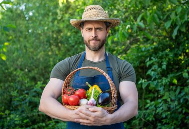 farmer in straw hat hold basket full of vegetables.