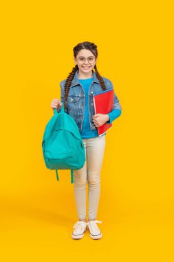 Happy teenage girl holding school bag yellow background. School education. Back to school.