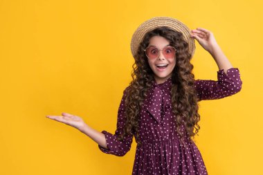 surprised happy child in straw hat and sunglasses with long brunette curly hair. copy space.