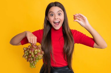 surprised girl hold fresh grapes fruit on yellow background.