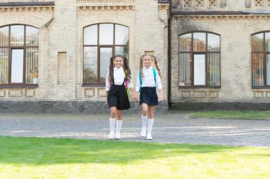 two schoolkids in uniform walking together outdoor.