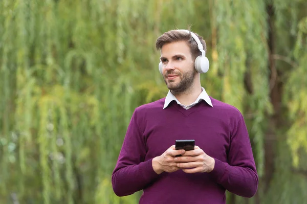 young handsome man listen music in headphones and chating on phone outdoor. copy space.