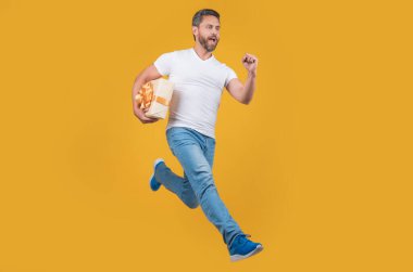 Energetic courier guy running with present box in midair yellow studio background. Courier service. Fast courier delivery.