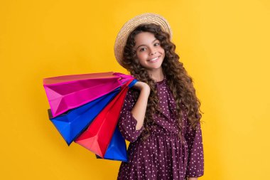 happy child with curly hair hold shopping bags on yellow background.