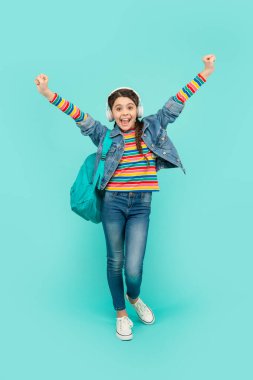 Happy teen girl making winning gesture blue background, school. Music school. Back to school.