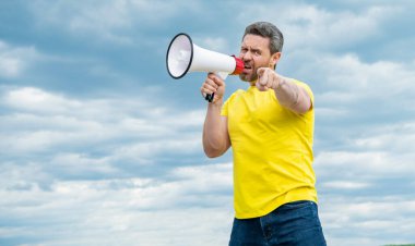 man in yellow shirt shout in megaphone on sky background. pointing finger.