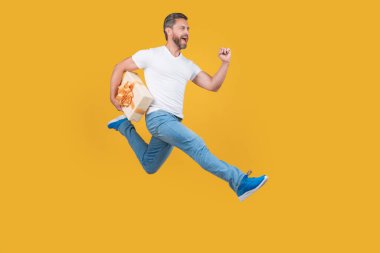 Energetic courier man running with gift box in midair yellow studio background. Fast courier delivery. Courier service.