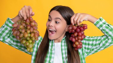 amazed teen kid with fresh grapes bunch on yellow background.