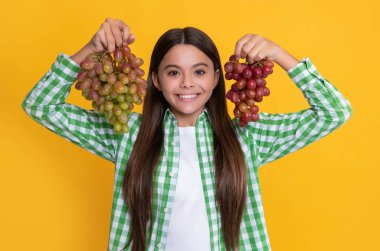 cheerful teen kid with grapes bunch on yellow background.