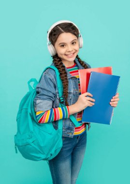 Happy teen girl listening to audio lesson blue background. Teenager listening to audiobook in headphones. Listening skills. School education.