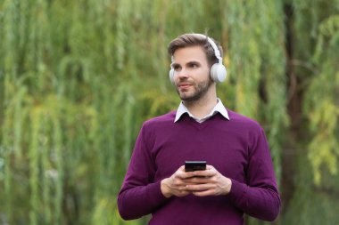 young handsome guy listen music in headphones and chating on phone outdoor.
