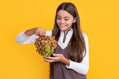 glad girl hold fresh grapes fruit on yellow background.