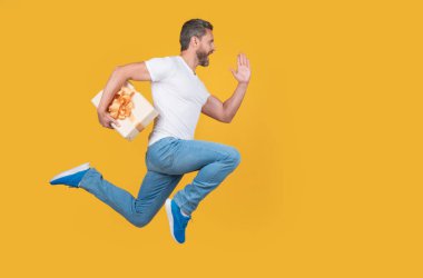 Active man running to deliver present box. Delivery boy in midair yellow studio background. Express delivery service. Fast delivery, copy space.