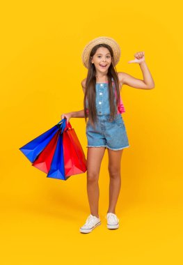 happy teen kid pointing on shopping bags on yellow background. full length.