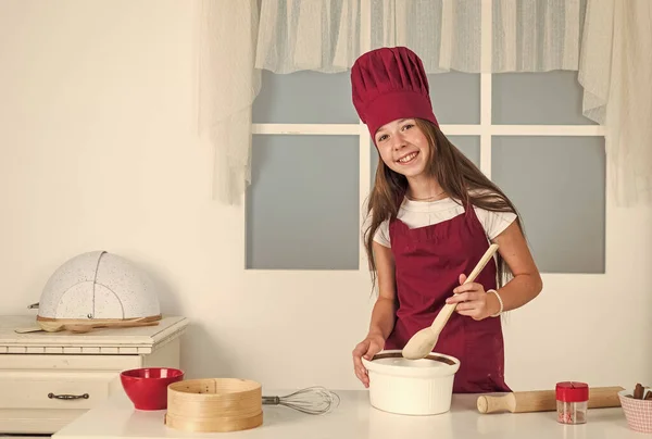 Feel fine dining. childhood development. small girl baking in kitchen. kid chef cooking with wooden spoon. child prepare healthy food at home and wearing cook uniform. housekeeping and home helping.
