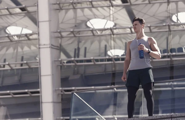 运动员英俊男子休闲喝水 现代体育场建筑背景 — 图库照片