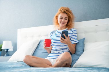 Telefonda internette kahve sörfü yapan mutlu bir kadın. Evde telefonuyla internette sörf yapan bir kadın. Kadının evinde internet sörfü.