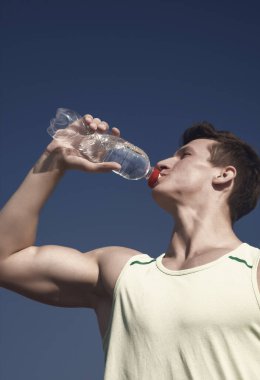 Mavi gökyüzü üzerinde yeşil tshirt atlet. Adam içme suyu şişe güneşli. Spor ve fitness kavramı. Vücut kas el kasları pazı, triceps ile. Sağlıklı yaşam ve sağlık.