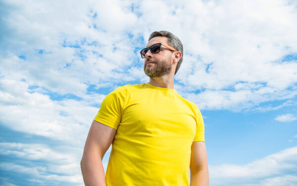 man wearing yellow shirt and sunglasses outdoor on sky background.