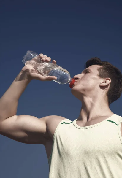 青い空に緑の シャツの選手 男は晴れた日にボトルから水を飲む スポーツとフィットネスの概念 筋肉手の筋肉上腕二頭筋 上腕三頭筋とボディービルダー 健康的なライフ スタイルと健康 — ストック写真