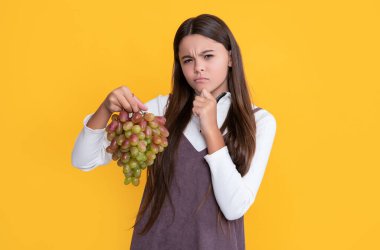 Düşünen çocuk sarı arka planda taze üzüm meyvesi tutuyor..