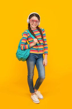 Okuldan sonra müzik dinleyen mutlu genç kız sarı arka plan, eğitim. Müzik eğitimi. Resmi olmayan eğitim.