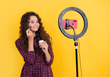 Uzun kıvırcık saçlı mutlu çocuk blogda toz fırçası tutma videosu yapıyor.