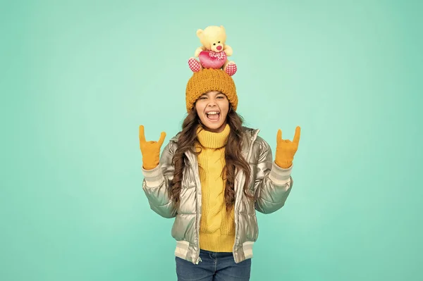 childhood. teen girl hold toy bear. child wearing warm clothes on blue background. express positive emotion. winter fashion. love toy for valentines day. cool emotional kid in puffer jacket and hat.