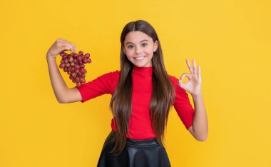 Genç çocuk gülümsüyor. Sarı arka planda bir demet üzüm var..