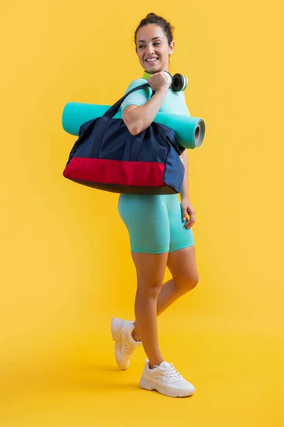 smiling fitness woman in sportswear with sport bag in studio. fitness woman in sportswear isolated on yellow background. fitness and sportswear.
