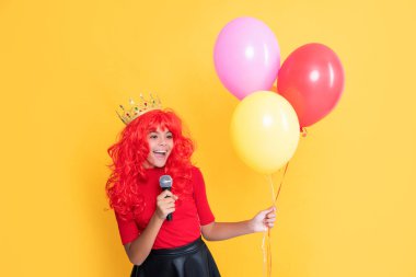 Sarı arka planda mikrofonlu ve parti balonlu mutlu çocuk..