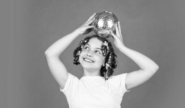 Retro parti. Çocuk altın disko topu tutuyor. Disko topu olan neşeli bir kız. Saç bigudileriyle poz veren modacı çocuk. Gece kulübü. Kuaför salonu. Süslü ergen. Disko partisi için saç stili. İyi eğlenceler..
