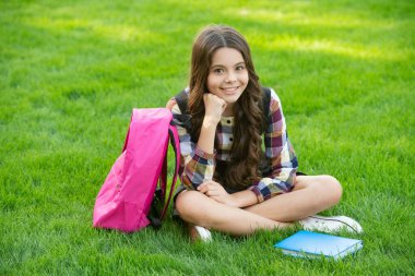 Okuldan sonra çimlerin üzerinde oturan mutlu genç kız, eğitim. Okula dönüyorum. Okul zamanı öğrenci..