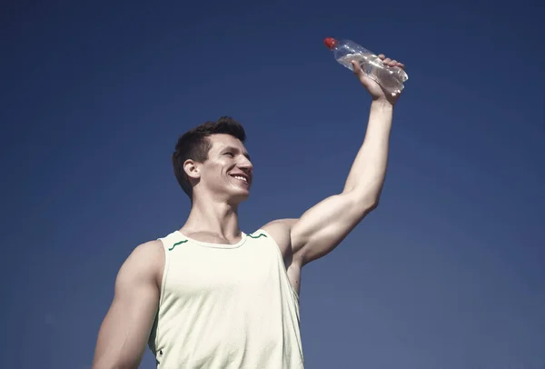 青い空に緑の シャツに笑みを浮かべて選手 筋肉手に水のボトルを持つ男 健康的なライフ スタイルと健康 スポーツとフィットネスの概念 ボディービルダーの筋肉上腕二頭筋 上腕三頭筋の晴れた日に — ストック写真