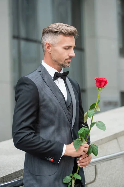 elegant man in black tuxedo. man wearing tuxedo bowtie outdoor. handsome tuxedo man with red rose.