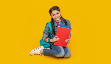 Dizlerinin üzerinde oturan mutlu genç kız sarı arka plan, okul. Okula dönelim. 1 Eylül. Okul eğitimi.
