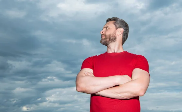 Confident guy sky background. Serious guy keeping arms crossed. Grizzled guy in casual outdoors, copy space.