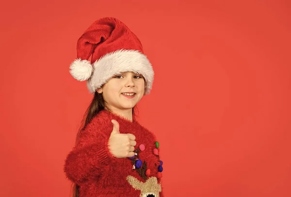 little santa helper show thumb up. small girl santa claus hat red background. copy space. ready for new year party. christmas my favorite holiday. love winter holidays. in xmas mood.