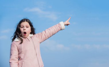 Gökyüzü arka planında şaşkın yüz parmağı olan çocuk.