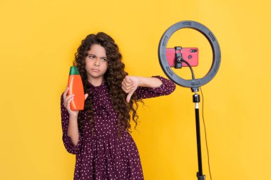 Uzun kıvırcık saçlı çocuk, blog şampuanı için video çekiyor. başparmak aşağı.