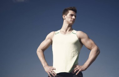 Adam vücut geliştirmeci mavi gökyüzü üzerinde poz. Güneşli yeşil tshirt atlet. Sağlıklı yaşam konsepti. Kas eller, pazı, triceps, kasları ile fitness modeli. Egzersiz ve eğitim, kopya alanı