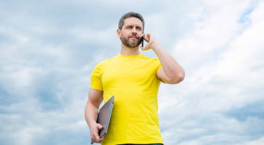 Bilgisayarlı bir adam gökyüzünde akıllı telefondan konuşuyor..