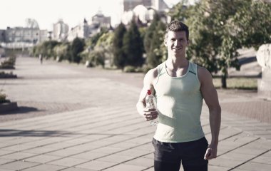 Eşofman su şişe üzerinde güneşli yaz günü açık havada bulanık kentsel peyzaj gülümseyerek mutlu bir adam atlet. Spor ve fitness. Sağlıklı yaşam konsepti.