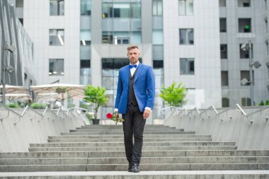 Smokinli zarif bir damat. Dışarıda smokin giyen bir damat. Kırmızı güllü yakışıklı damat..