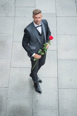 Smokinli şık bir adam. Dışarıda papyonlu takım giyen bir adam. Kırmızı güllü yakışıklı smokinli adam..