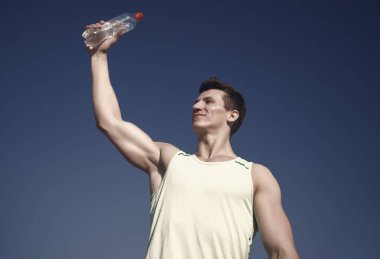 Vücut kas, pazı, triceps güneşli. Mavi gökyüzü üzerinde yeşil tshirt atlet. Spor ve fitness kavramı. Sağlıklı yaşam ve sağlık. Kas elinde su şişesi ile mutlu adam.