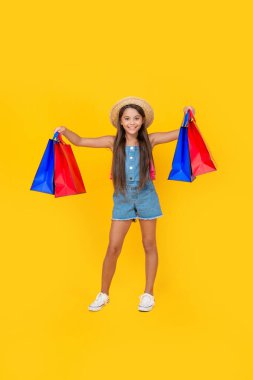 Sarı arka planda alışveriş torbaları olan mutlu ergen çocuk alışverişi. tam uzunluk.