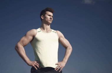 Kas eller, pazı, triceps, kasları ile fitness modeli. Güneşli yeşil tshirt atlet. Sağlıklı yaşam konsepti. Egzersiz ve eğitim. Mavi gökyüzü, kopya alanı poz adam vücut geliştirmeci