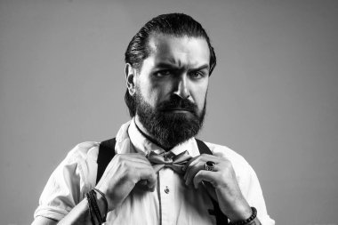 Bıyıklı vahşi sakallı adam pantolon askısı ve papyon takıyor, modası geçmiş gibi görünüyor..